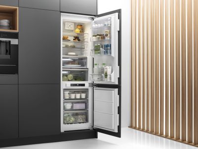 Ein moderner Kühlschrank mit offenem Tür, gefüllt mit Lebensmitteln und Getränken, steht in einer Küche mit Holzjalousien.